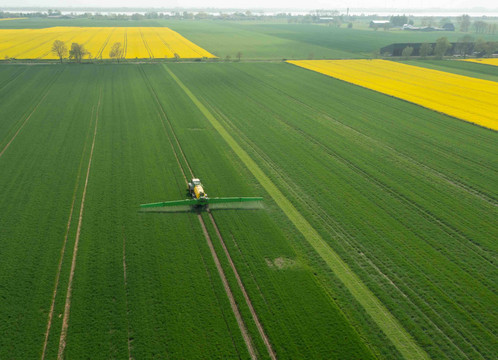 Aus der Luft ist ein Traktor auf landwirtschaftlich genutzten Flächen zu sehen, der Pflanzenschutzmittel versprüht