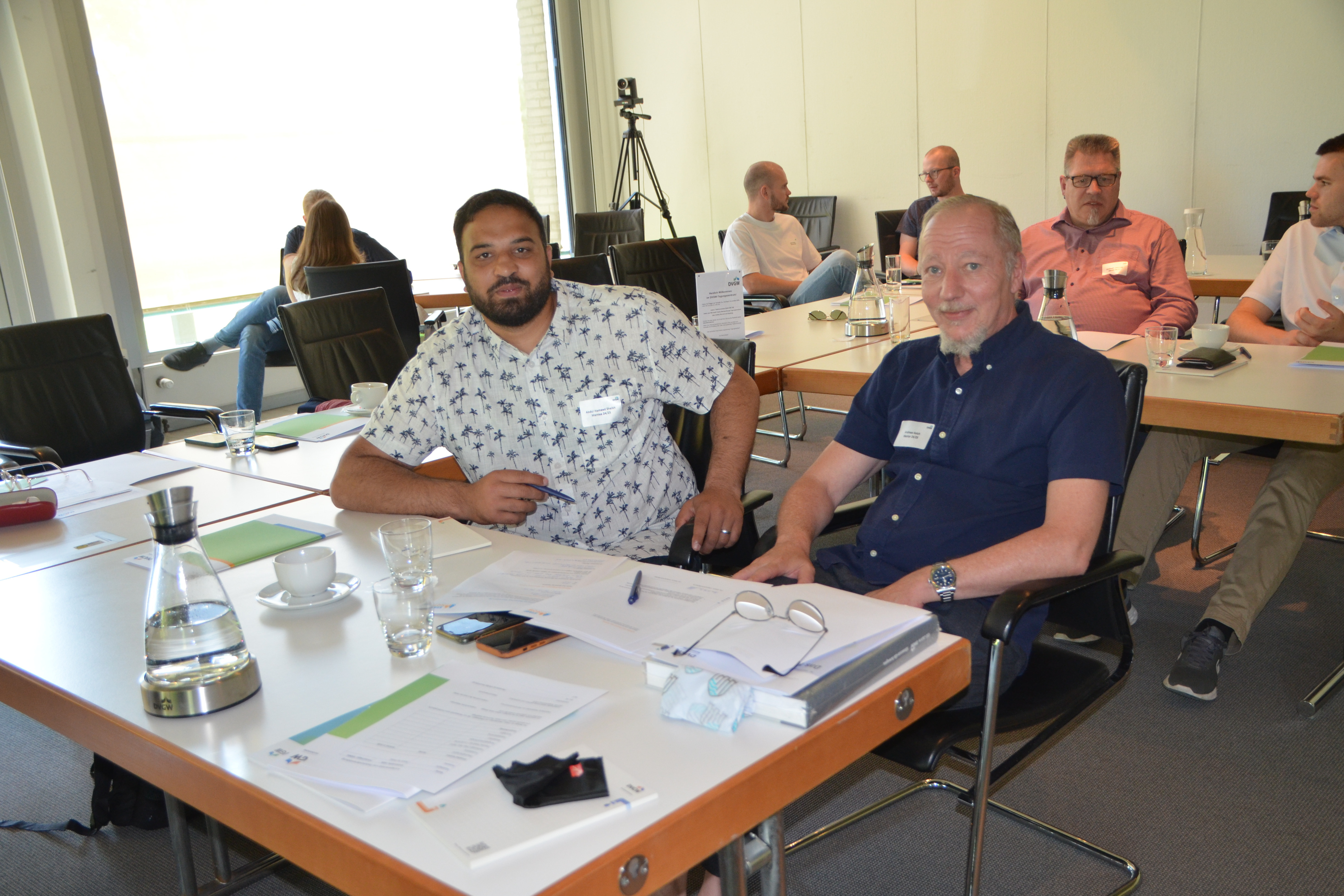 Menschen sitzen in Zweiergruppen an Konferenztischen